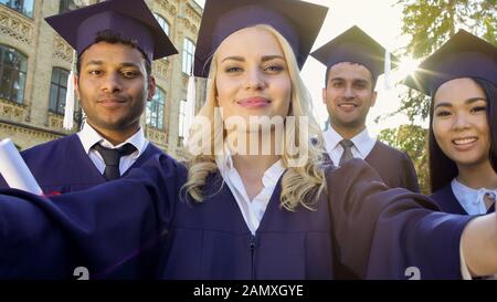 Students in academic regalia taking selfie on graduation day, achievement Stock Photo