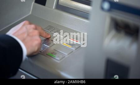 Businessman entering his pin code on keyboard of ATM, banking services, finance Stock Photo
