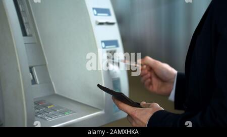Business man inserting credit card in ATM to receive money, withdrawing cash Stock Photo