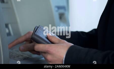 Man with purse inserting card in ATM to withdraw cash and receive balance report Stock Photo