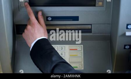 Mans hand pressing button on display screen of ATM machine, bank account access Stock Photo
