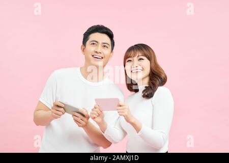 Image of excited couple man and woman smiling while both using mobile phones isolated over pink background Stock Photo