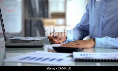 Businessman accountant using calculator and filling report near laptop at office Stock Photo