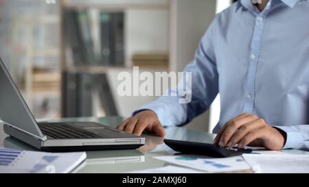 Office manager working on company sales report, using laptop and calculator Stock Photo