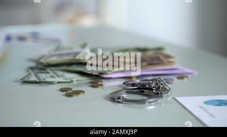 Handcuffs and money on table, bribery punishment, financial control system Stock Photo