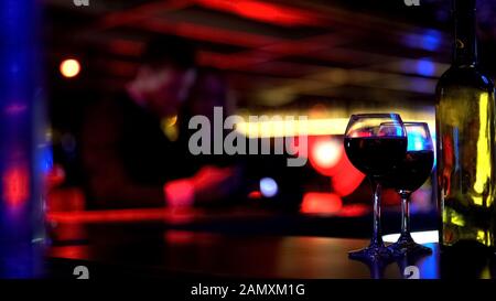 Two glasses of wine and bottle at bar in nightclub, couple on blurred background Stock Photo