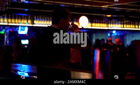 Man dancing alone at bar counter and drinking alcohol, watching people in club Stock Photo