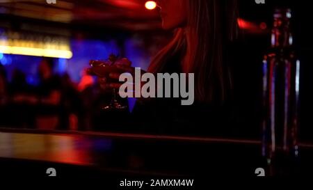 Elegant woman drinking cocktail in bar alone, enjoying music, relaxed atmosphere Stock Photo