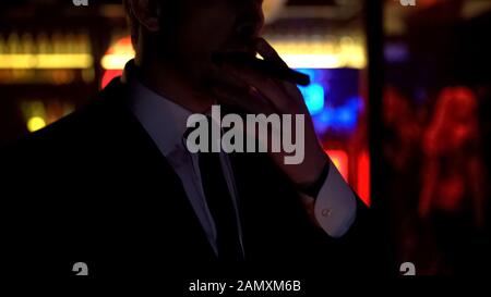 Successful businessman smoking cigar, enjoying evening in elite strip club Stock Photo