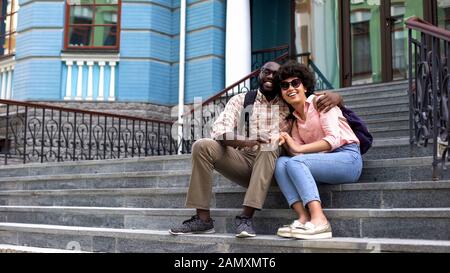 Happy student couple hugging, sitting on university building stairs, youth love Stock Photo