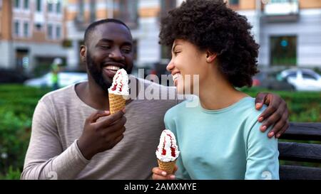 Dating couple eating ice-cream, sitting on city bench, having fun together, love Stock Photo