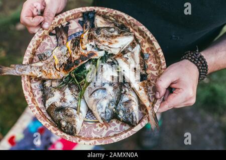 A man holds a plate with a ready meal. delicious and fresh grilled fish with lemon on the Barbeque grill at the garden in summer. Selective focus macr Stock Photo