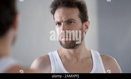 Middle aged man looking at mirror reflection, dissatisfied with skin condition Stock Photo