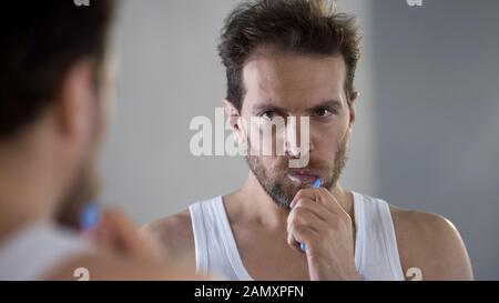 Sleepy man brushing teeth, tired of routine, going to work in morning, hangover Stock Photo