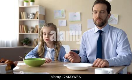 Pretty girl and her father praying before eating breakfast, spiritual education Stock Photo