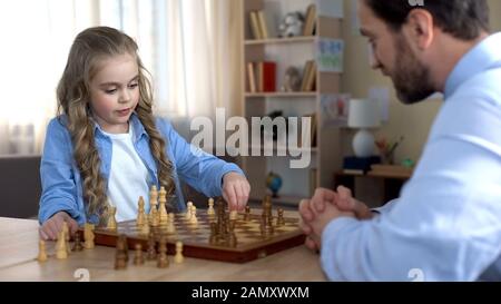 Little daughter thinking over next move, playing chess with father, strategy Stock Photo