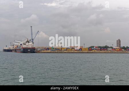 General Cargo vessels and Container Ships, loading and unloading cargo at the busy Port of Conakry in Guinea on an overcast November Morning. Stock Photo