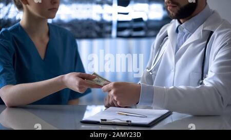 Young doctor giving bribe to head physician, corruption in medicine, close up Stock Photo
