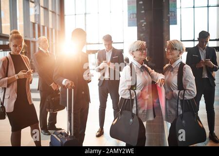 Group of people with luggage using their gadgets while standing in a queue at the airport Stock Photo
