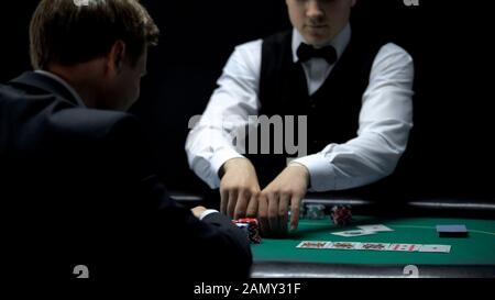 Casino croupier giving businessman all chips for winning at poker, gambling Stock Photo