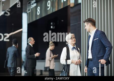 Senior businesswoman in eyeglasses talking to the young employee while they standing at the airport and they are going to business trip Stock Photo