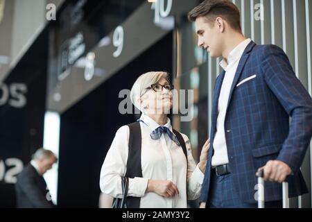 Senior businesswoman talking to the young businessman with luggage before his flight at the airport Stock Photo