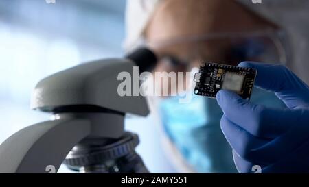 Technician examining chip, using microscope to run diagnosis and upgrade device Stock Photo