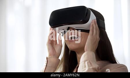 Young woman using futuristic VR technology and laughing, pleased with imagery Stock Photo