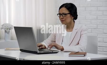 Middle-aged lady boss working on laptop, successful and confident businesswoman Stock Photo