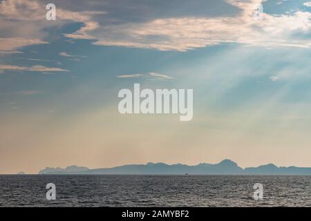 Dramatic sun rays hitting the sea off the coast of Thailand. Hills of Phi Phi Island can be seen in the background. Stock Photo