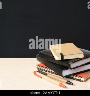 Notebooks and pens on wooden table with school black board for background Stock Photo