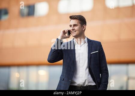 Smiling young businessman in formalwear has a conversation on mobile phone in the city Stock Photo