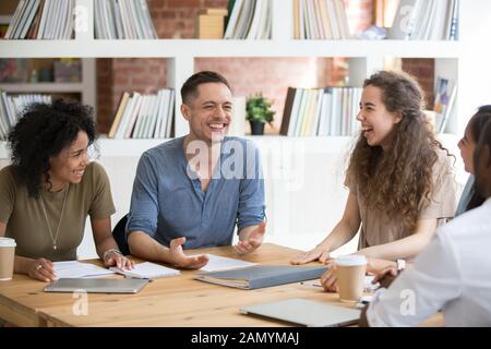 Smiling multiracial millennial colleagues laugh talking at meeting Stock Photo