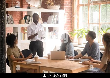 Black millennial man stand talking collaborating with diverse group Stock Photo