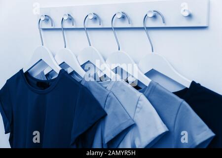 T-shirts of different shades of classic blue hang on a hanger in a store. Selection and sale of clothes in a shopping center. Color of the year 2020 c Stock Photo