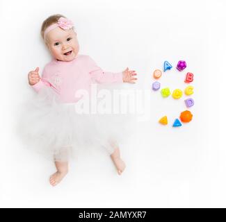 Portrait of a sweet infant baby girl wearing a pink dress and headband bow, isolated on white in studio with number nine from toys Stock Photo