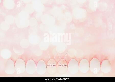 Decorated Easter eggs with cute bunny face and ears drawn on over a pastel pink background with bokeh and free space for text. Image shot from top vie Stock Photo