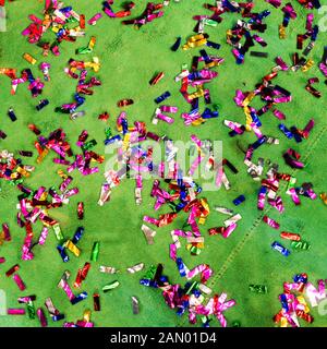 Scattered pieces of confetti on a green surface. Multi-colored and shiny ribbons after the holiday. The end of a holiday, birthday or anniversary. Stock Photo