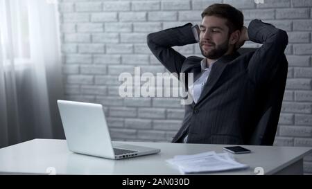 Handsome businessman smiling after successful online deal, lucrative contract Stock Photo