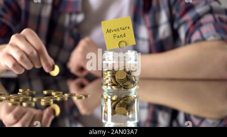 Adventure fund phrase above glass jar with money, savings for hobby, interests Stock Photo