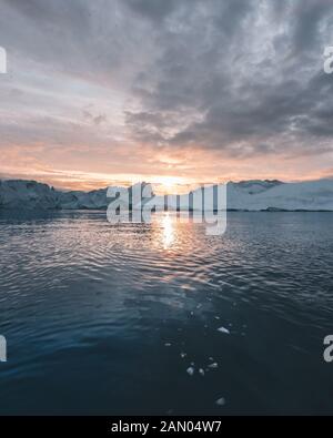 Arctic nature landscape with icebergs in Greenland icefjord with midnight sun sunset sunrise in the horizon. Early morning summer alpenglow during Stock Photo