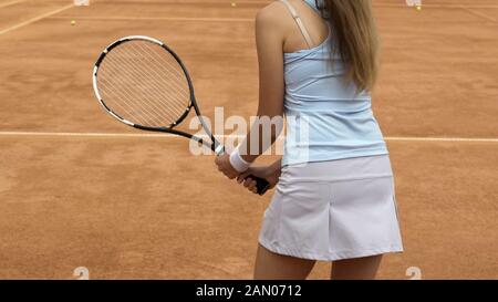 Slim female athlete jumping and preparing to hit tennis ball on court, closeup Stock Photo