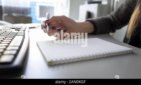 Female hand holding pen, taking notes in her notebook, searching for data on PC Stock Photo