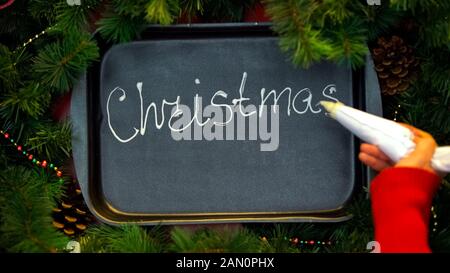 Christmas, woman writing word with cream on baking tray, fest celebration Stock Photo