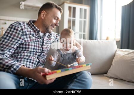 Father in a checkered shirt watching his daughter playing xylophone Stock Photo