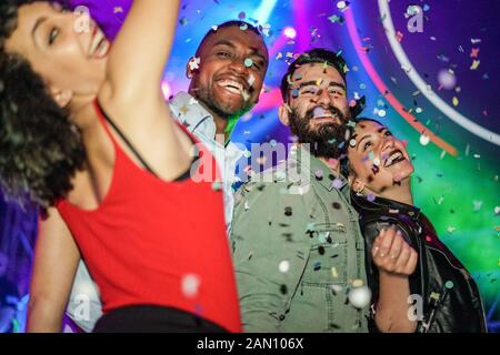 Happy friends having fun in night club dance floor with canon ball throwing confetti - Young people enjoying weekend nightlife - Focus on bearded whit Stock Photo