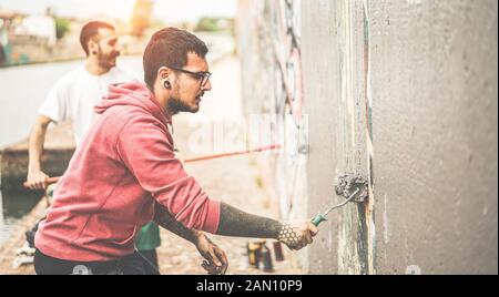 Two writers covering the wall with grey color before painting their picture - Contemporary artists at work - Urban lifestyle, street art and youth con Stock Photo