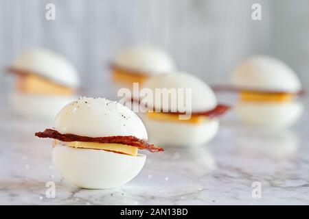 Keto BLT egg sandwich, or egg bun snack for the ketogenic diet plan. Boiled eggs with turkey bacon and cheddar cheese. Selective focus with blurred ba Stock Photo