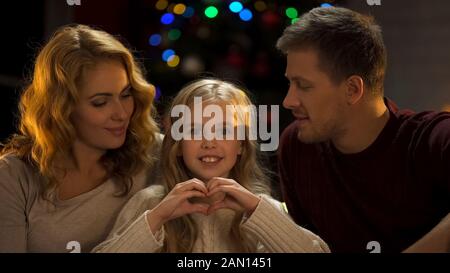 Daughter making heart of hands, celebrating Christmas with parents, family love Stock Photo