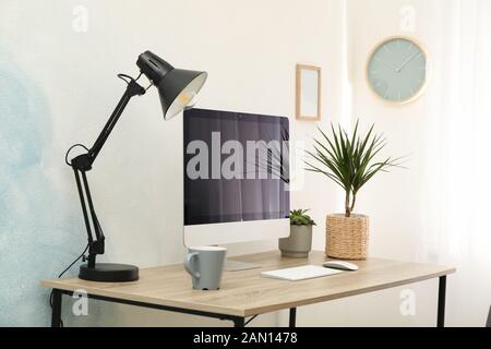 Workplace with computer, plants and lamp on wooden table. Empty black screen Stock Photo